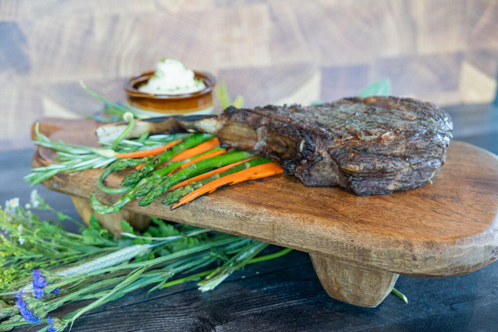 t-bone steak atop grilled asparagus and carrots on wood block