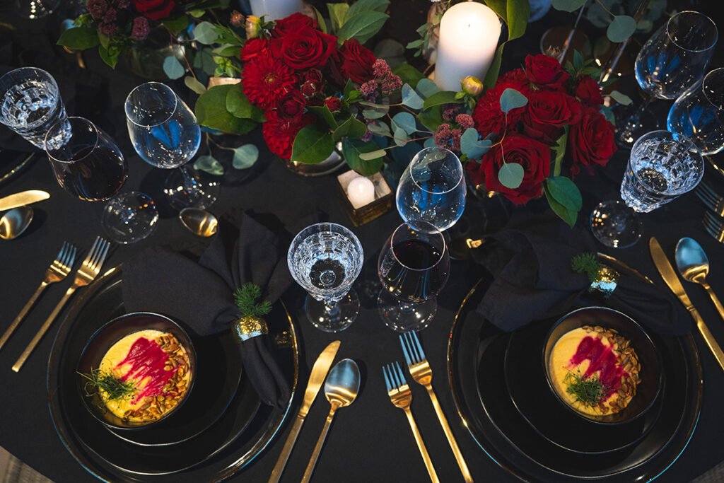 Black table setting with black stoneware showcasing butternut squash soup, served with gold cutlery, crystal clear glassware and roses.