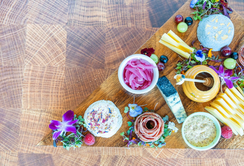 charcuterie board with fruit, flowers, meats, and cheeses